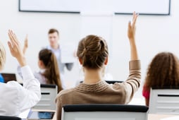 student raising hand to answer question in class